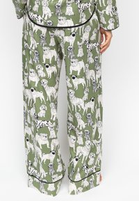 Groene pyjama set met verschillende hondenillustraties in zwart-wit. De broek heeft een losse pasvorm en zwarte bies langs de zoom.