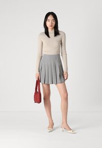 Beige ribbestrikket langermet topp, grå plissert skjørt med hvite prikker, rød håndveske, hvite spissede hæler. Minimalistisk design.