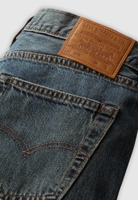 Denimjeans med en mørkeblå vask, der har orange syninger, et læderbagstykke med præget branding og et klassisk fem-lommers design.
