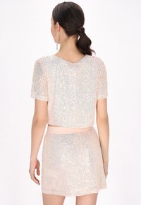 Conjunto de top corto de mangas cortas y falda mini hecho de lentejuelas iridiscentes con base en rosa suave, que presenta un escote redondo y una cintura elástica.