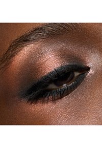 Gros plan sur un œil avec un eyeliner noir et des fards à paupières cuivrés. Texture de peau lisse avec une finition scintillante. Les cils sont définis et foncés.