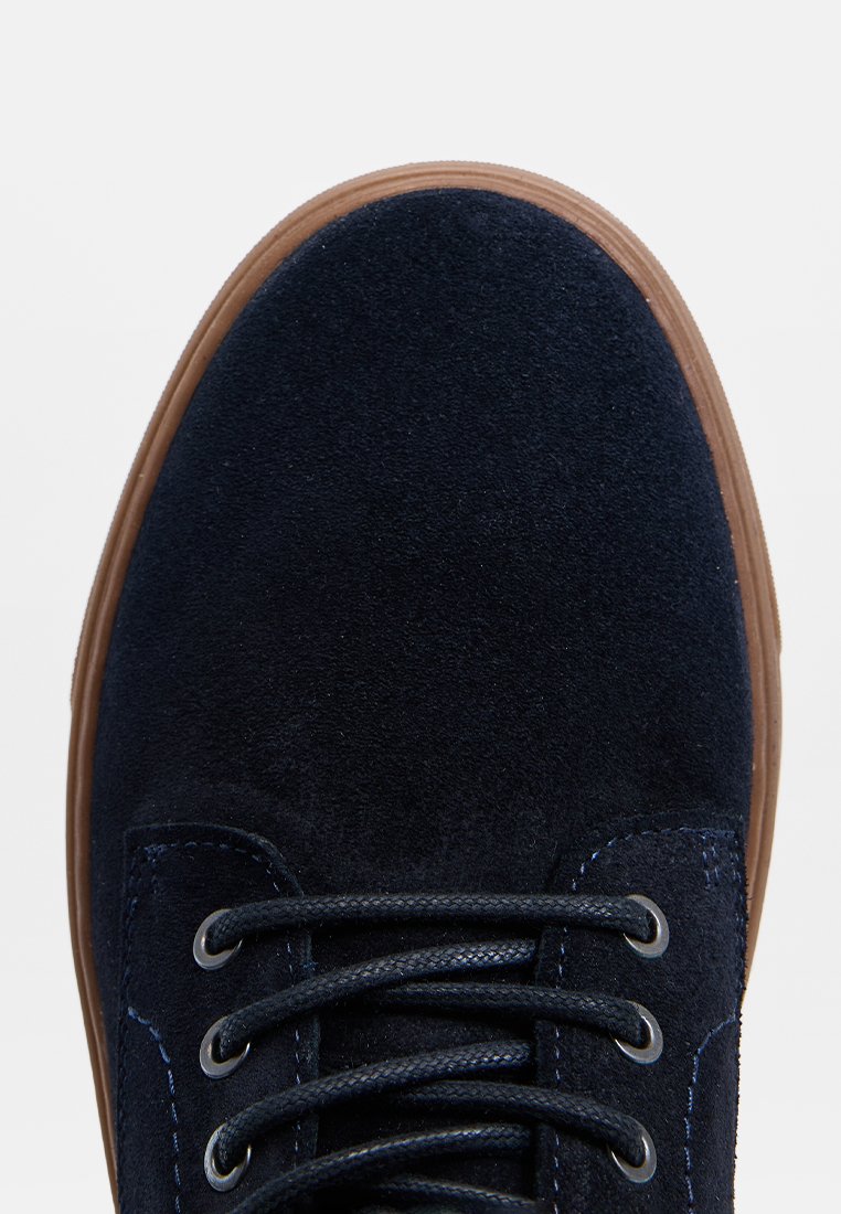 Marineblaue Wildledersneaker mit runder Zehenform, flachem Schnürdesign, kontrastierender brauner Gummisohle und gestickten Details entlang der Ösen.