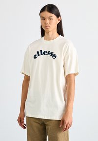 Camiseta de algodón de manga corta en color crema con cuello redondo y un logo "ellesse" en azul marino en el pecho.
