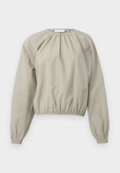 Beige cropped blouse with elasticized waist and cuffs, featuring a gathered neckline and lightweight, slightly textured fabric.