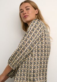 Printed dress featuring a black background with cream and gold fan patterns. Long sleeves gathered at the cuffs, lightweight fabric with flowy design.