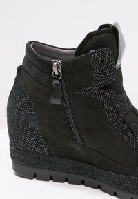 Baskets compensées noires en suède et matériaux texturés, avec une fermeture éclair latérale et des accents circulaires, présentant un design élégant.