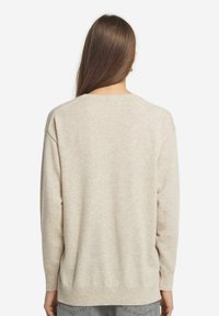 Beige gestrickter Pullover mit lockerem Schnitt, langen Ärmeln und geripptem Saum. Die Textur wirkt weich und glatt.