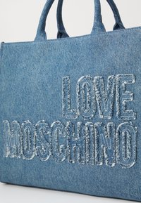 Denim tote väska med framträdande "LOVE MOSCHINO" text i fransad broderi. Blå färg med strukturerad yta och dubbla handtag.