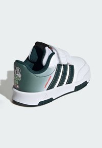 Scarpe da ginnastica bianche con tre strisce verdi, dettagli neri e un tallone grigio. Presentano una grafica di un personaggio dei cartoni animati sul retro. Chiusura con velcro.