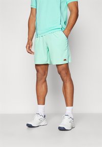 Shorts atletici de un verde mentă deschis, cu o textură fină, cu un tiv contrastant navy și un logo brodat. Asortați cu un tricou corespunzător și pantofi albi.