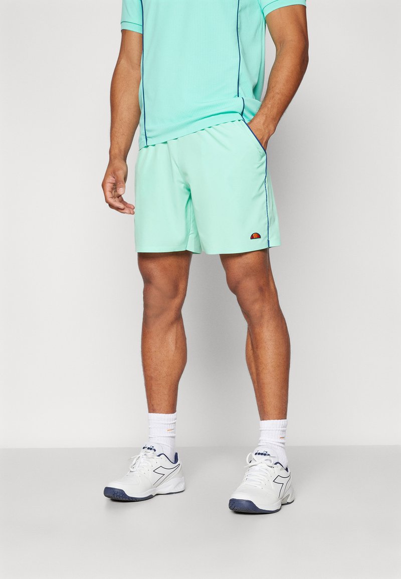 Shorts atletici de un verde mentă deschis, cu o textură fină, cu un tiv contrastant navy și un logo brodat. Asortați cu un tricou corespunzător și pantofi albi.