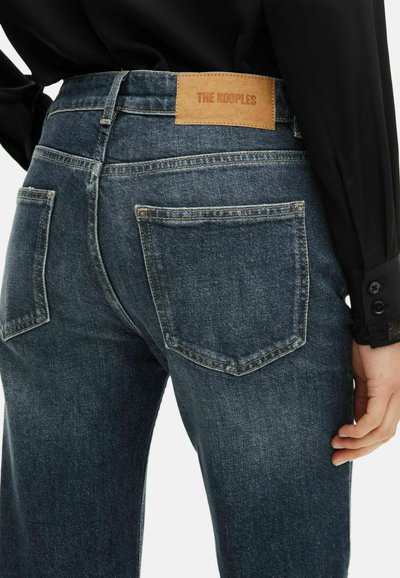Pantalones vaqueros de un azul oscuro con un acabado texturizado, que cuentan con dos bolsillos traseros y un parche de piel marrón en la cinturilla.