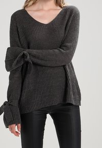 Pull gris foncé côtelé avec col en V et manches longues, avec des accents noués aux poignets. Fabriqué en maille texturée.