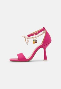 Vaaleanpunaiset korkokenkä-sandaalit, joissa on ohut nilkkaremmikin, ja joissa on kultaketju, johon on kiinnitetty viehättäviä riipuksia, kuten flamingo, ananas ja kirsikat.