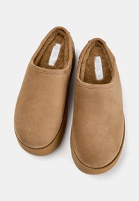 Barna velúr slip-on cipők, puha bélés belsővel és vastag gumi talppal. Kerek orrúak, látható fűzők vagy fémszálak nélkül.