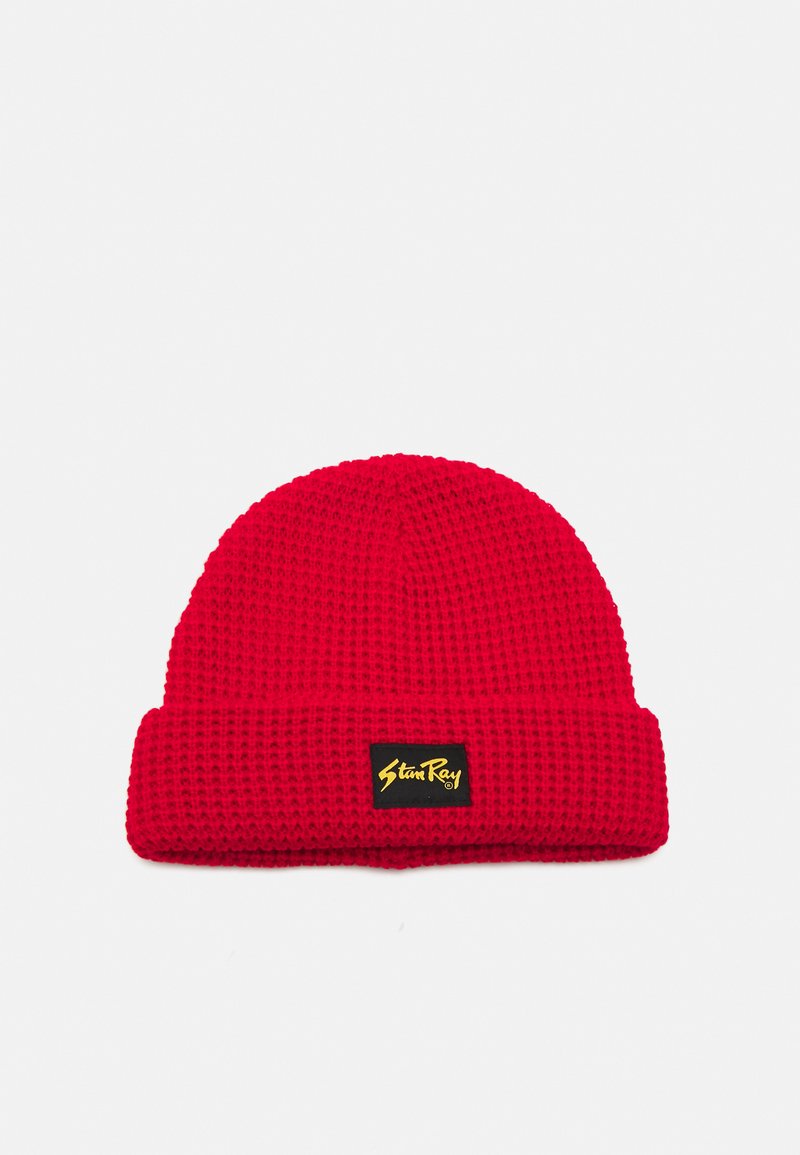 Căciulă tricotată roșie cu un model texturat, având un eticheta neagră cu numele brandului în galben. Design cu tiv la baza.