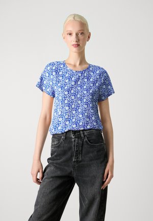 Haut à manches courtes à motif floral bleu avec un col rond, fabriqué en tissu léger, associé à un jean noir taille haute.
