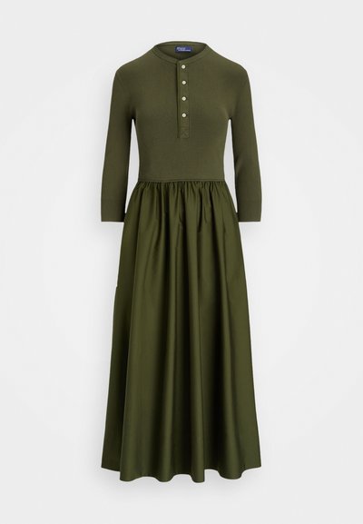 Vestido de malha em verde oliva com parte superior canelada, mangas três-quartos e saia plissada com pregas. Apresenta um fecho de botões e gola redonda.