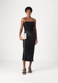 Robe en satin noir avec des bretelles fines et un corsage ajusté, descendant jusqu'à une longueur midi. Associée à une pochette beige et des sandales noires avec des accents en métal.