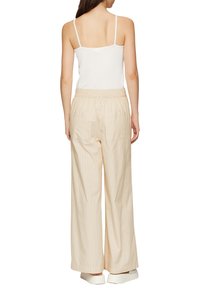 Wit geribbeld tanktop gecombineerd met lichtbeige wijde broek met een elastische tailleband en twee achterzakken met een gestreepte textuur.