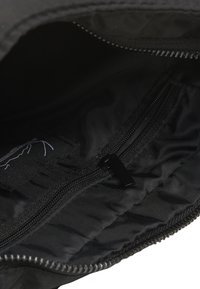 Juodas audinio maišelis su užtrauktuku; tekstūruota vidinė pamušalo danga ir papildoma kišenė su užtrauktuku; turi logotipą.