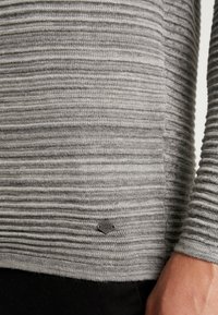 Gray striped knit sweater featuring a textured design, long sleeves, and a small logo tag near the hem. Soft fabric with ribbed pattern.