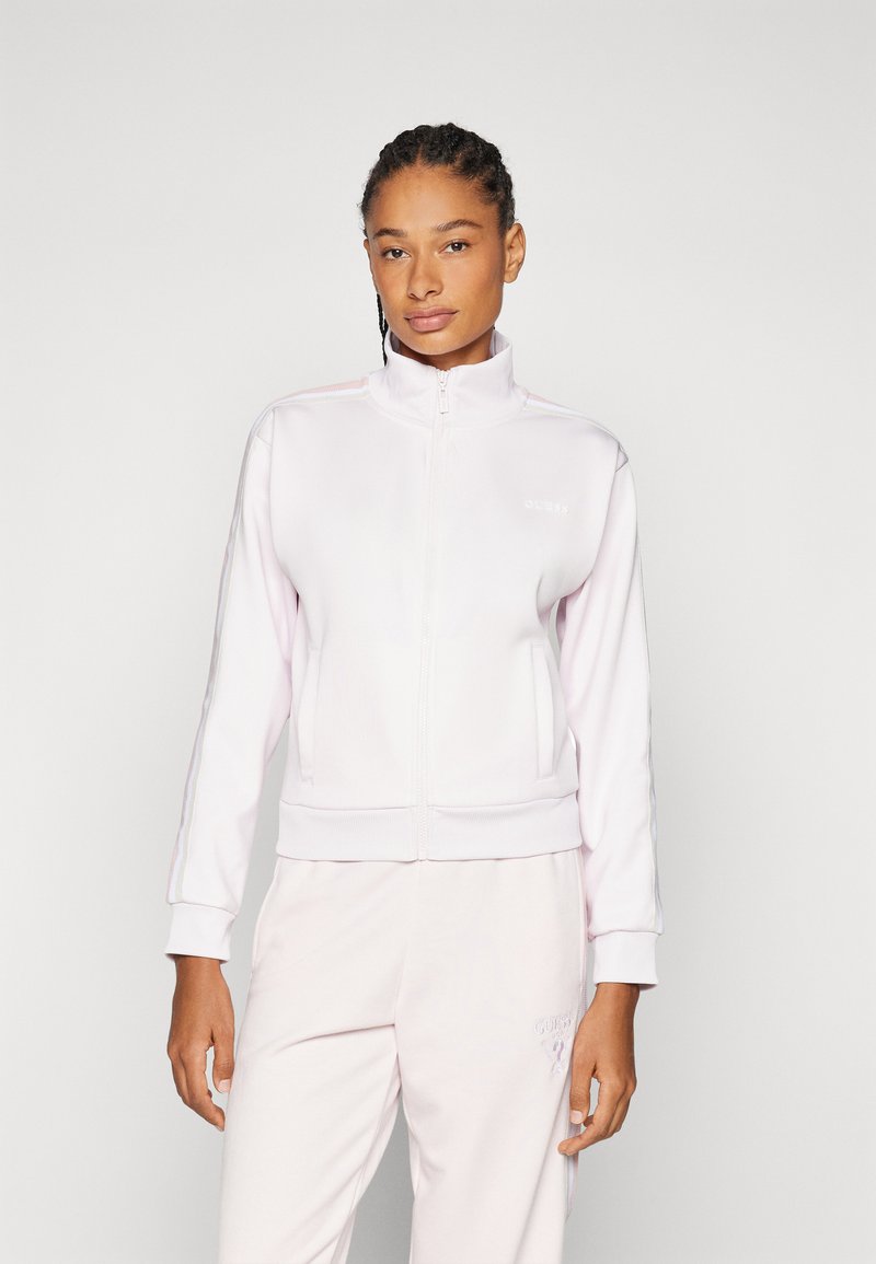 Chaqueta de cremallera rosa claro con un cuello alto, que presenta bolsillos laterales y rayas texturizadas en las mangas. El material parece suave y elástico.