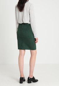 Grön mockapenskjorta med dragkedja bak, matchad med en vit och randig långärmad topp, samt svarta klackskor.