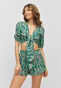 Set a fiori verdi composto da un crop top con maniche a sbuffo annodato e pantaloni corti a vita alta, entrambi realizzati in un tessuto leggero e morbido.