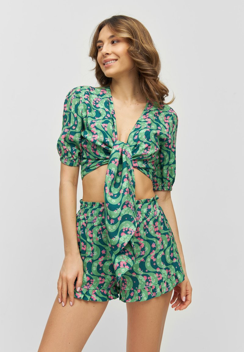 Set a fiori verdi composto da un crop top con maniche a sbuffo annodato e pantaloni corti a vita alta, entrambi realizzati in un tessuto leggero e morbido.