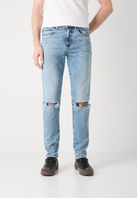 Lyseblå revnet jeans med frynset kanter, klassisk fem-lommers design og rett snitt. Kombinert med svarte joggesko for kontrast.