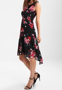 Czarna sukienka w kwiaty z dopasowaną górą, rozkloszowanym dołem i asymetrycznym hemem. Posiada wzory czerwonych i różowych kwiatów oraz cieniutkie ramiączka.
