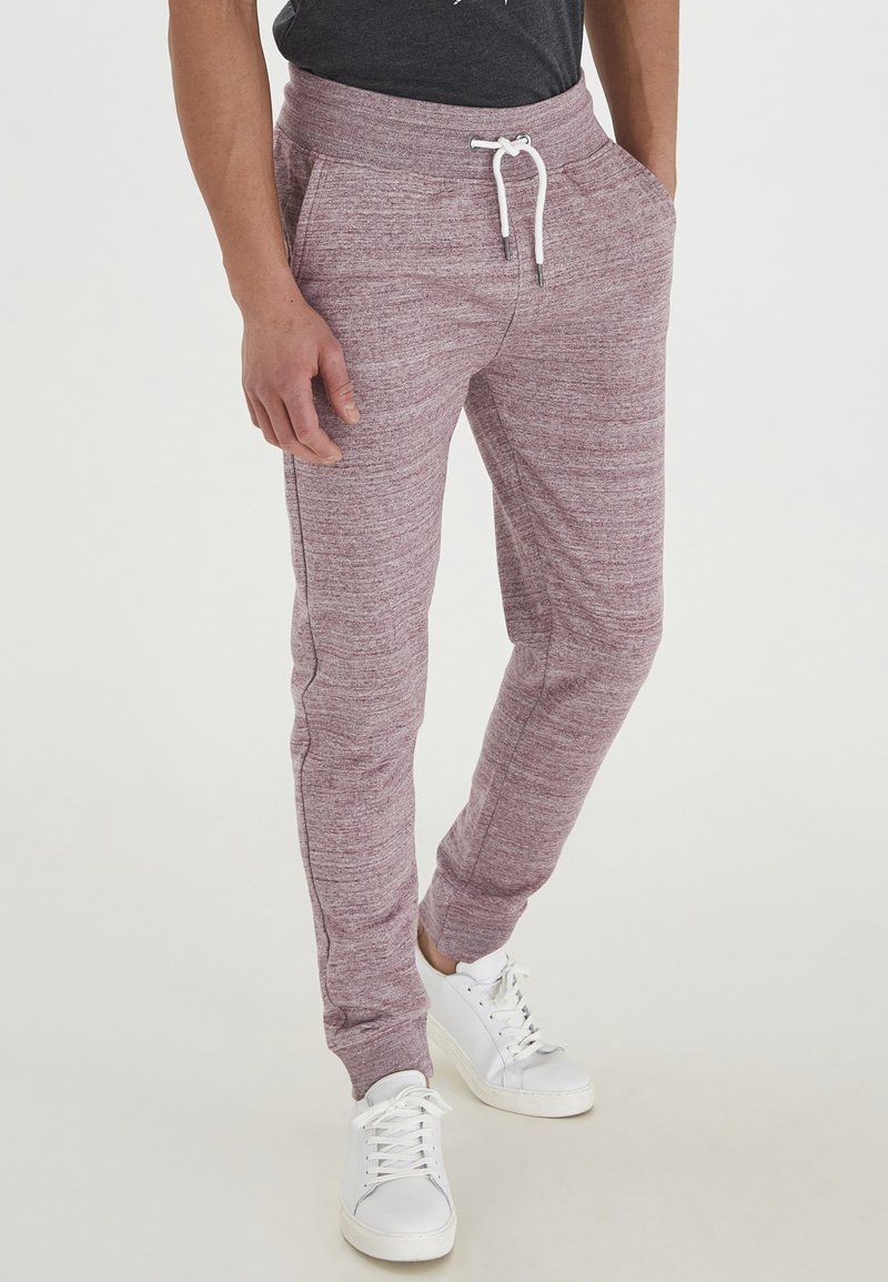 Bordeauxfarbene Jogginghose mit strukturiertem Strickfinish, ausgestattet mit einem Kordelzugbund und Seitentaschen, kombiniert mit weißen Sneakers.
