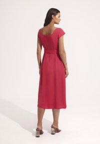 Sukienka do kolan z krótkim rękawem w jaskrawoczerwonym kolorze. Posiada kwadratowy dekolt z tyłu oraz dopasowaną talię z pasującym paskiem. Przezroczyste sandały na słupku.
