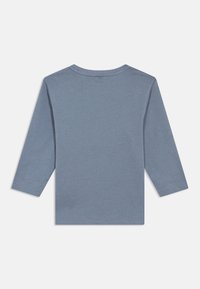 Camisa azul lisa de mangas longas com decote redondo, exibida deitada mostrando o lado de trás contra um fundo branco.