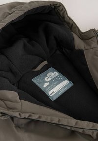Inner lining of a waterproof jacket with black fleece fabric and a sewn label featuring clouds, raindrops, and name tag fields.