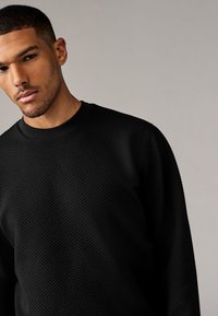 Schwarzer Sweatshirt mit Struktur, Rundhalsausschnitt und langen Ärmeln, ausgestattet mit einem Rautenmuster und einem glatten Innenfutter.