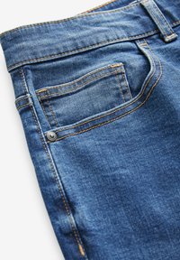 Blauwe denim jeans hebben een vervaagde afwerking, oranje stiksels en een klein voorvak. De stof is glad en heeft een klassiek vijfzakkenontwerp.