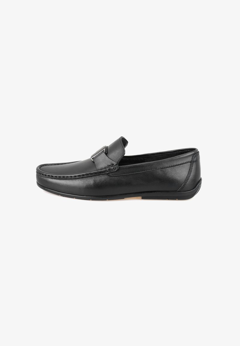 Mocassins en cuir noir avec un design de pointe cousu, présentant un détail de boucle décoratif et une forme lisse et arrondie. Semelle en caoutchouc.