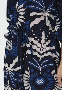 Navyblaues Kleid mit weißen und blauen Blumenmustern, Bindegürtel und fließender Stoffstruktur.