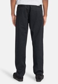Pantalon noir à jambes droites en coton avec une texture unie, doté de poches arrière et d'une ceinture. Porté avec des baskets noires.