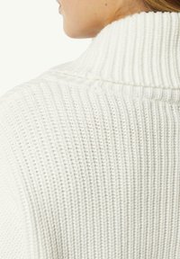 Weißer, gestrickter Pullover mit hohem Kragen und Rippenstruktur, der ein weiches, warmes Material und ein engmaschiges Muster zur Schau stellt.