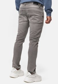 Vaqueros de mezclilla gris con cinco bolsillos, un corte ajustado y detalles sutiles de costura en los bolsillos traseros, combinados con zapatillas blancas.