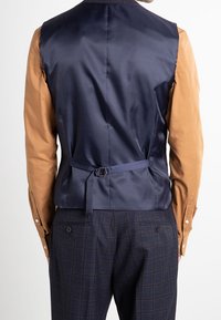 Marineblaues Satinweste mit schmalem Rückengurt, kombiniert mit einem rostfarbenen Hemd. Verfügt über eine glatte Textur und einen dezenten Glanz.