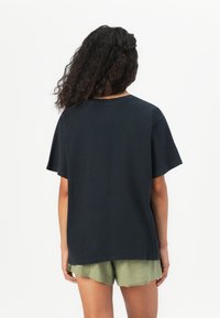 T-shirt en coton noir à manches courtes, coupe ample, encolure ronde et design uni. Associée à un short vert olive.