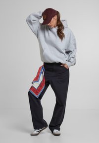 Šedá mikina s kapucňou, čierne nohavice širokého strihu so bočnými vreckami, dekoratívny červený a biely šál a šedé tenisky s čiernymi pruhmi.