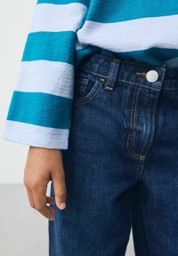 Tummansininen ja vaaleansininen raidallinen pitkähihaisotto, jossa on rakenteellinen pintakuvio, yhdistettyinä tummansinisii denim-farkkuihin, joissa on oranssia tikkausta ja metallinen nappi.
