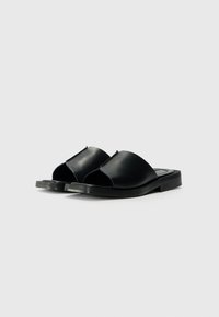 Svarta lädersandaler med öppen tå, med en slät yta och minimalistiska platta sulor. Ingen ytterligare hårdvara eller mönster.