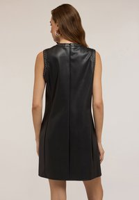 Vestido negro sin mangas hecho de cuero sintético, con acentos de tachuelas a lo largo de los hombros y una silueta ajustada y elegante.