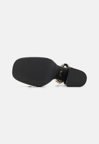 Soletta nera della sandaletta con superficie testurizzata; presenta una fibbia con accenti decorativi e una forma sagomata per il supporto. Design con tacco piatto.